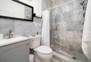 A bathroom with a marble shower wall, a toilet, and a sink.
