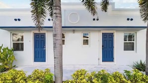 Un edificio blanco con puertas y ventanas azules, rodeado de follaje.