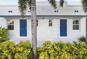 A white building with blue doors and windows, surrounded by greenery.