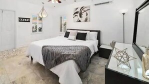 Un dormitorio con cama, mesita de noche, ventilador de techo, una obra de arte en la pared y una lámpara de pie.