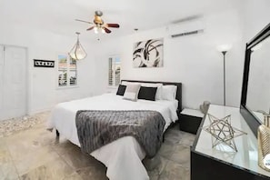 A bedroom with a bed, a nightstand, a ceiling fan, a wall-mounted artwork, and a floor lamp.