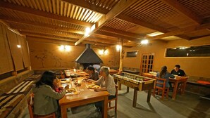 A cozy indoor dining area with wooden tables and chairs, a foosball table, and a large fireplace. - Terra Luna Lodge Atacama (San Pedro de Atacama)