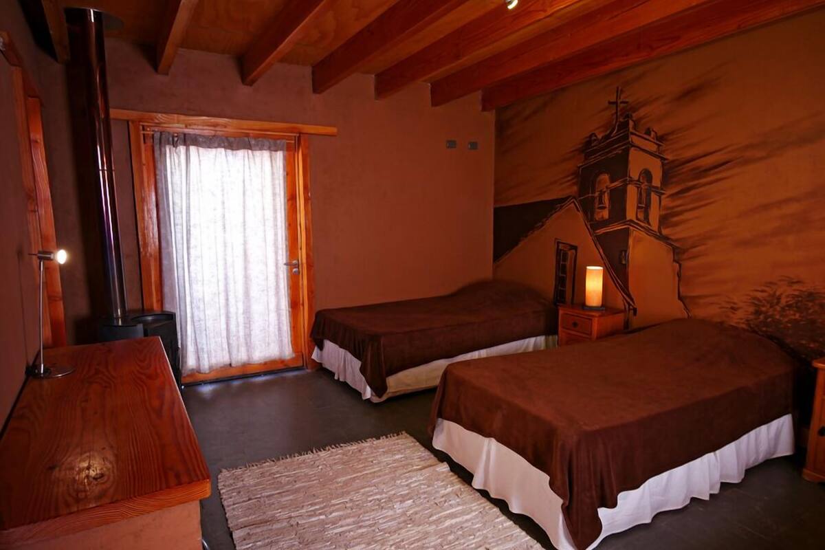 Una habitación acogedora con dos camas, una mesa de madera, chimenea y un ventanal con cortinas.