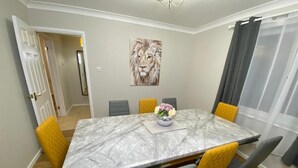 A dining area with a marble table, six chairs, a vase of flowers, and a lion painting on the wall. - Spacious 4 bedroom house close to all the main activities in Colchester (Colchester)
