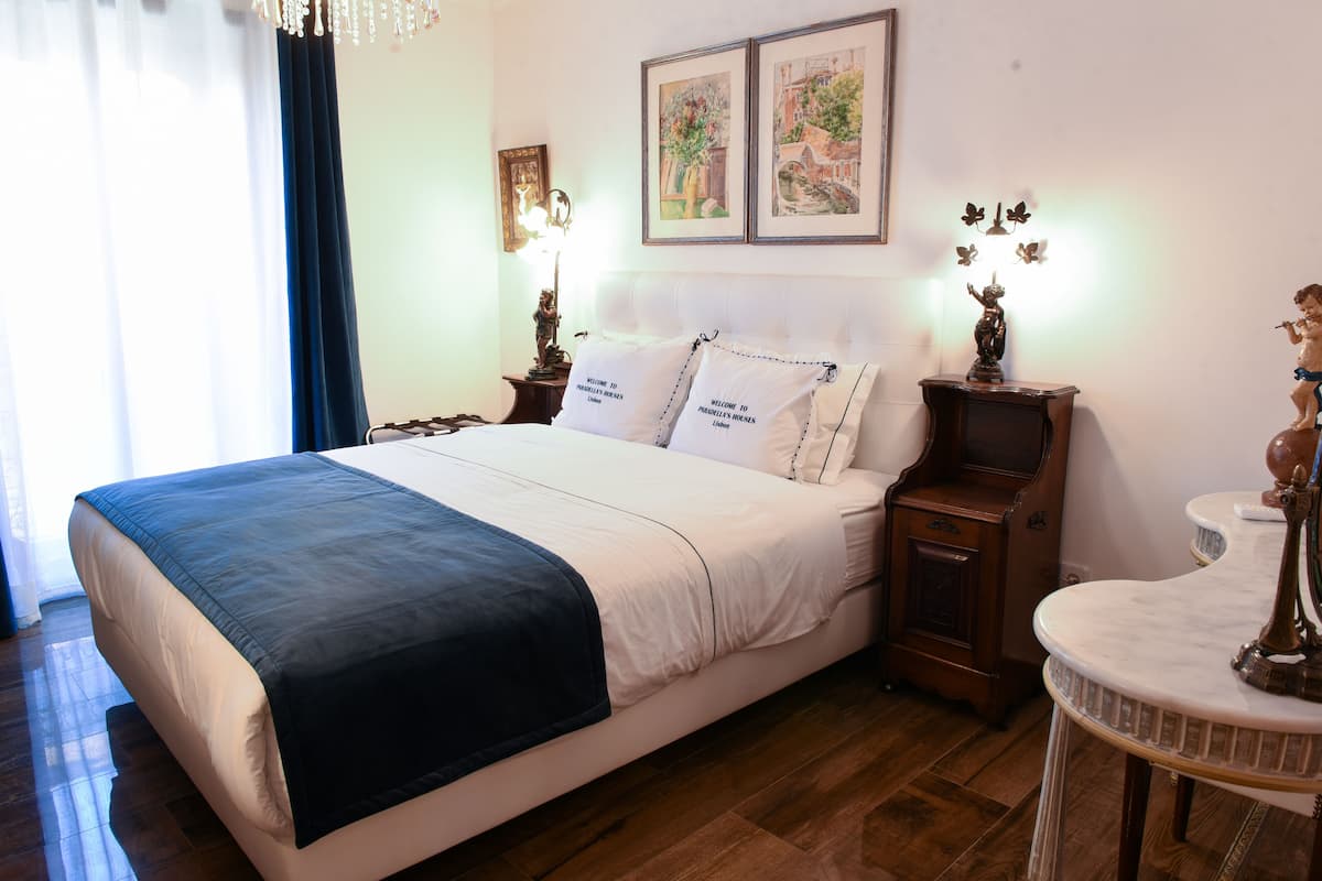 A neatly made bed with a blue blanket, a nightstand with a lamp, and a small table with a decorative item.