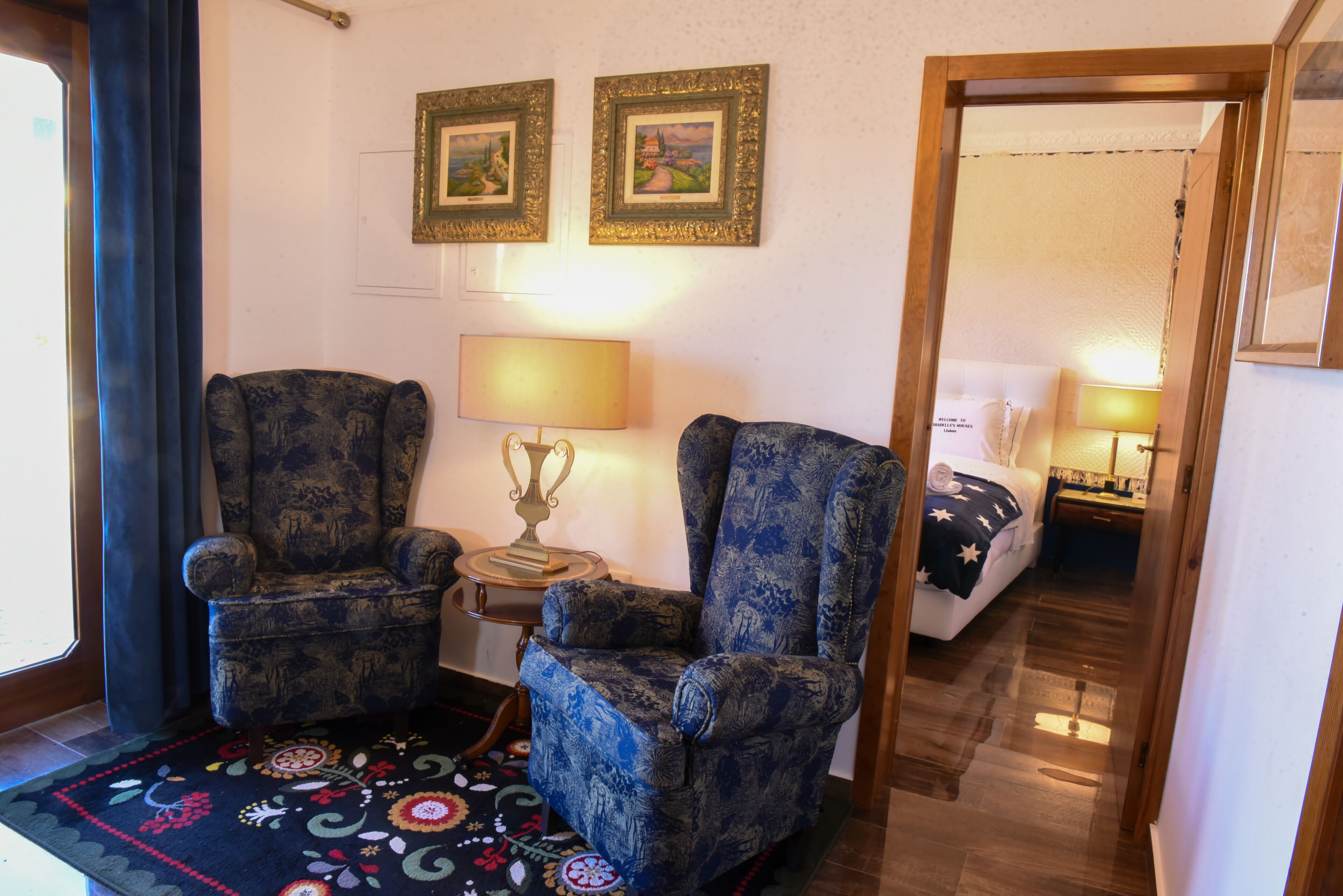 Una habitación con dos sillones, una mesita con una lámpara y una cama con una colcha estampada de estrellas.