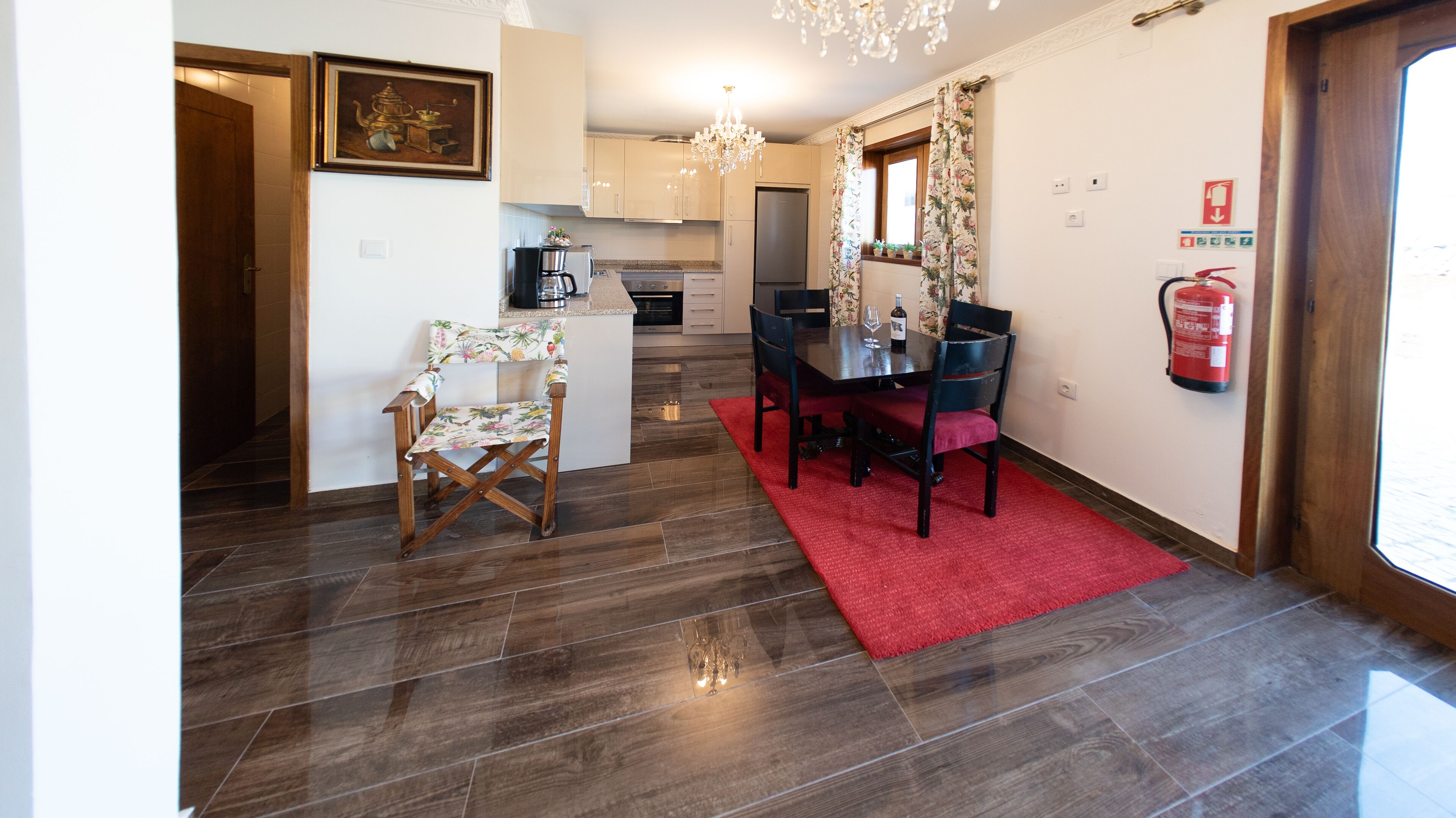 A modern kitchen with a dining area, wooden flooring, and a red rug.