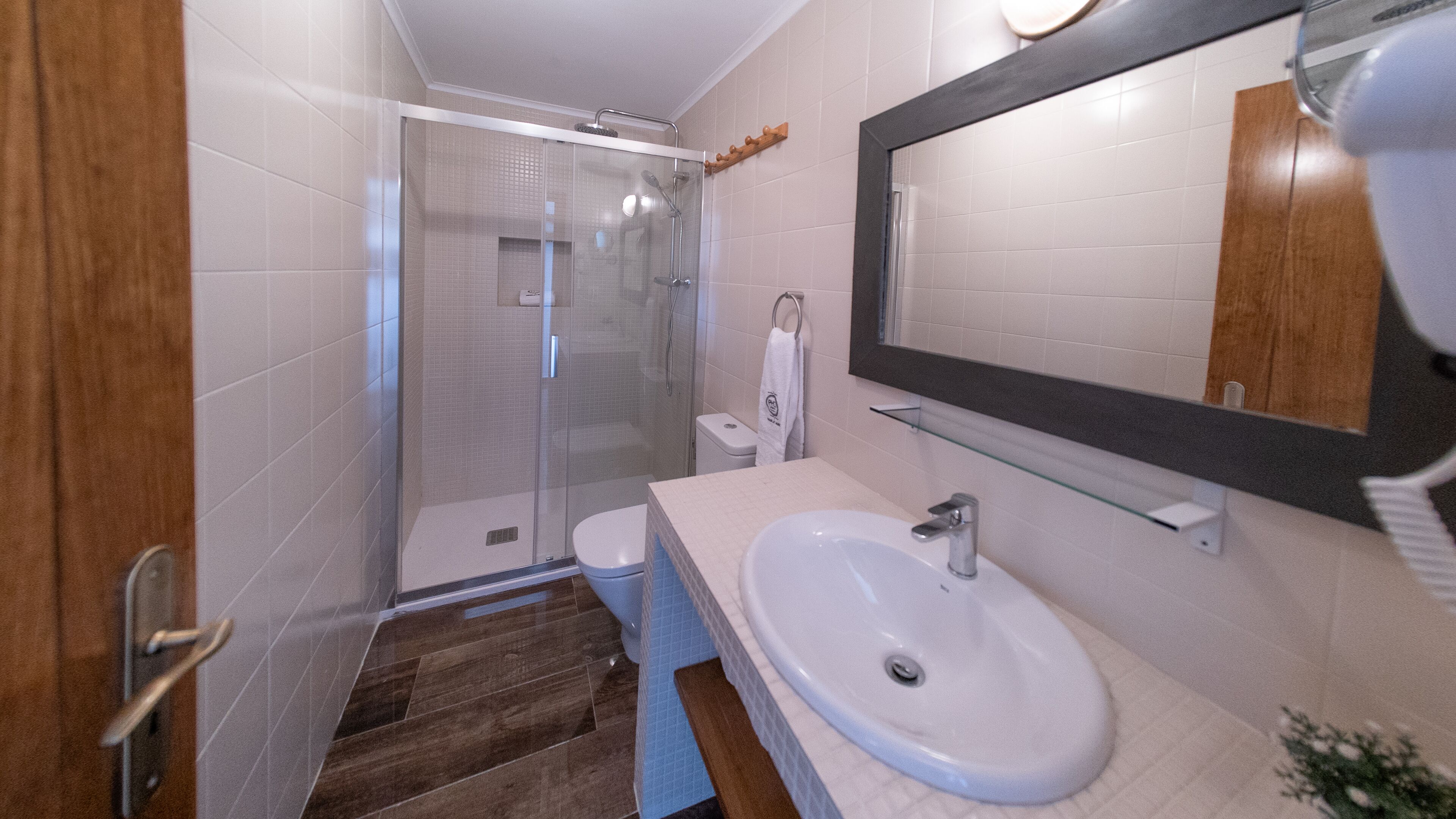 Un baño moderno con cabina de ducha de vidrio, un lavabo blanco y un espejo grande.