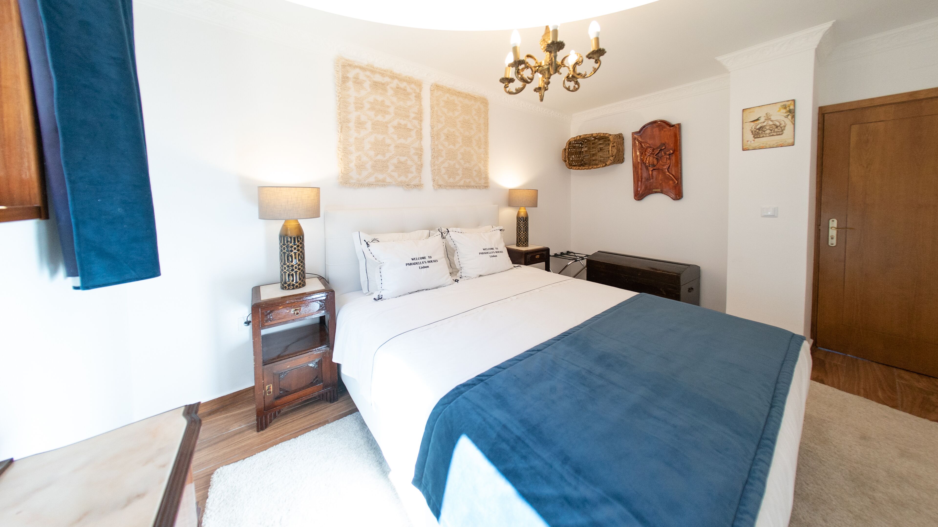 A bedroom with a large bed, two bedside tables, a chandelier, and a wardrobe.