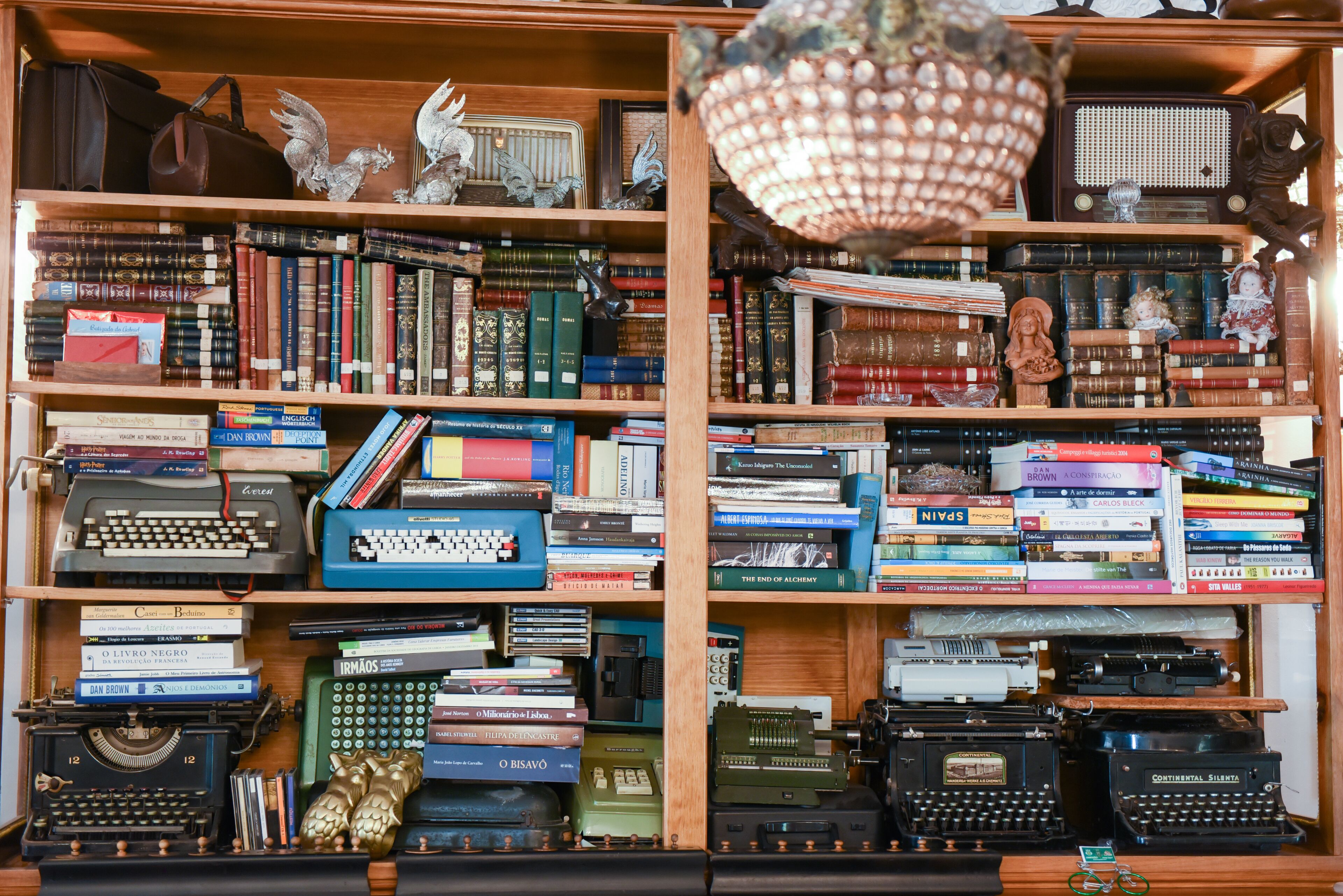 Una estantería llena de libros, máquinas de escribir y objetos decorativos.