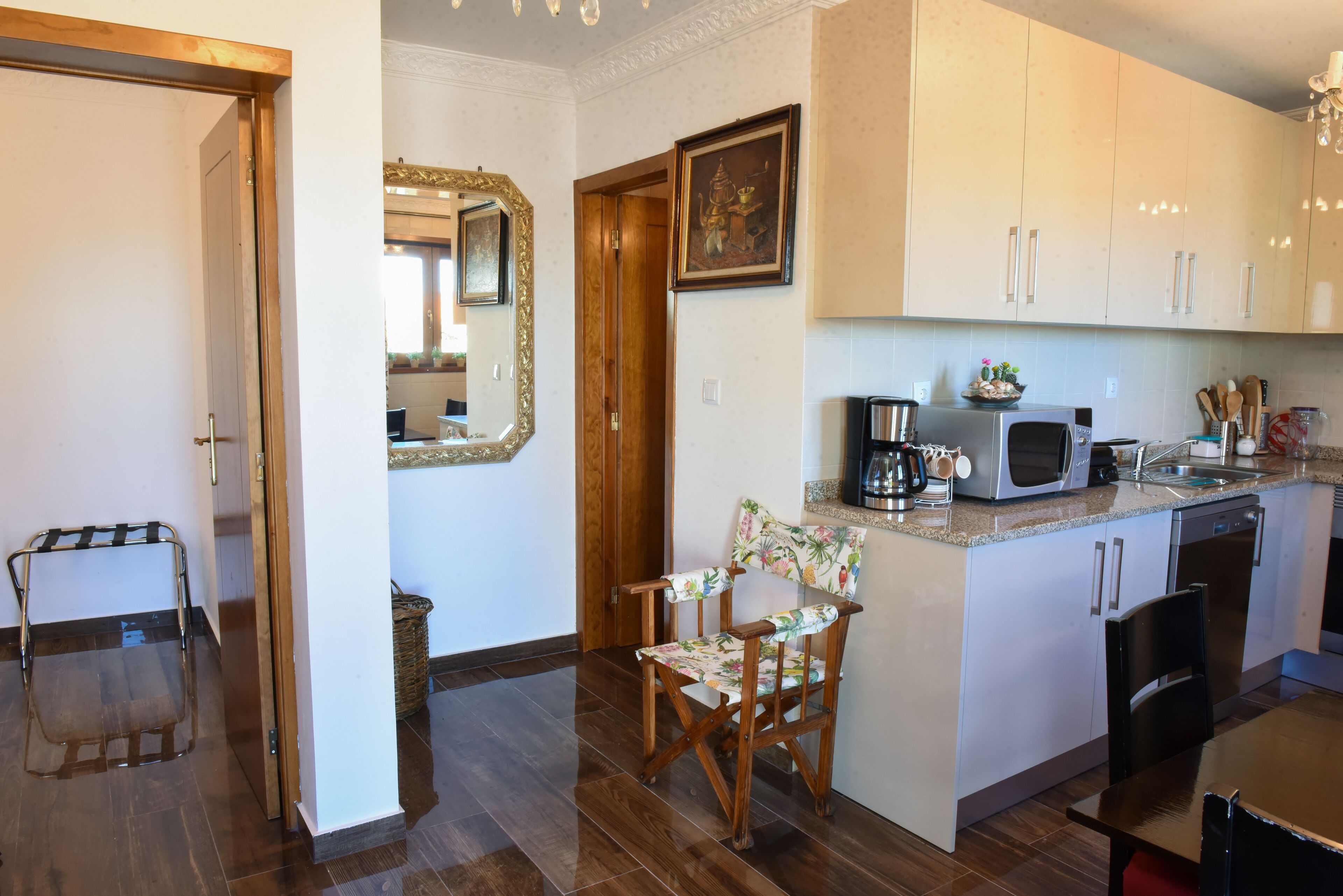 Cocina compacta con microondas, tostadora y lavabo. Se ve una silla de madera y una mesa pequeña.