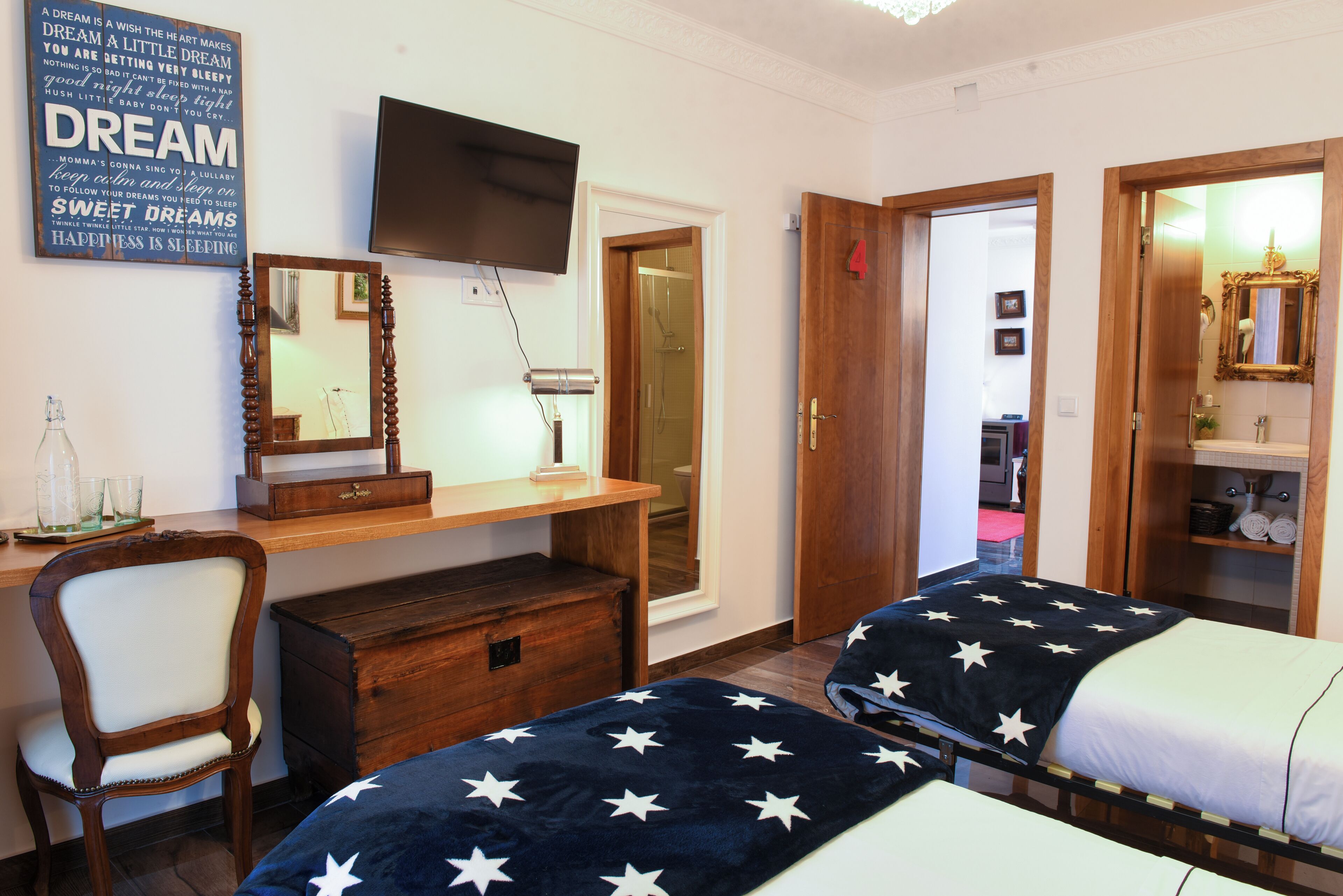 A bedroom with two beds, a desk, a chair, a TV, and a door leading to another room.