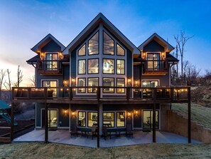 Une maison à deux étages dotée d’un balcon, de grandes fenêtres et d’un espace extérieur aménagé pour s’asseoir.