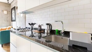 Une cuisine moderne avec des meubles blancs, un plan de travail en granit, un évier en acier inoxydable et une cuisinière à gaz.