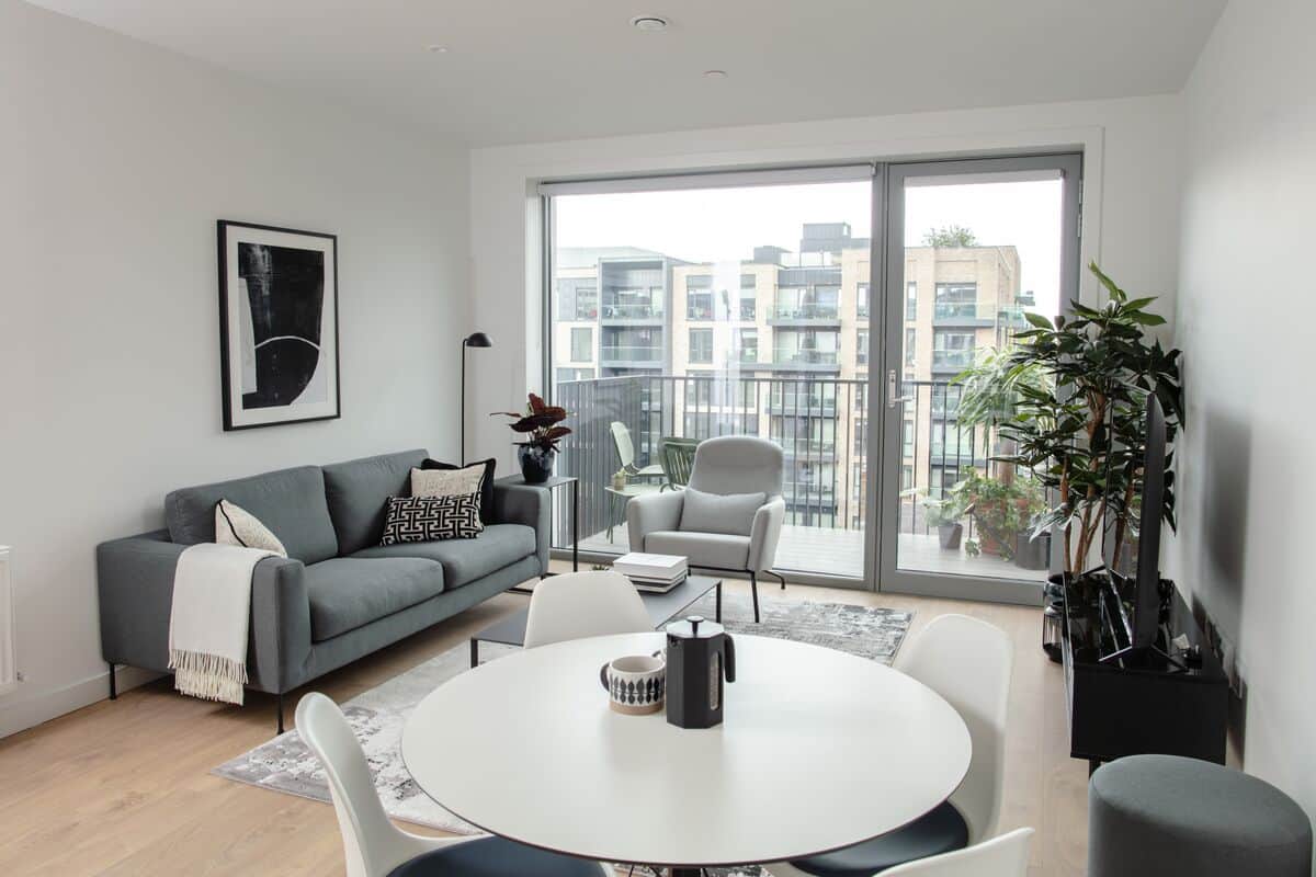 Ein modernes Wohnzimmer mit einem grauen Sofa, weißen Sesseln, einem runden Tisch und einem großen Fenster mit Blick auf die Stadt.