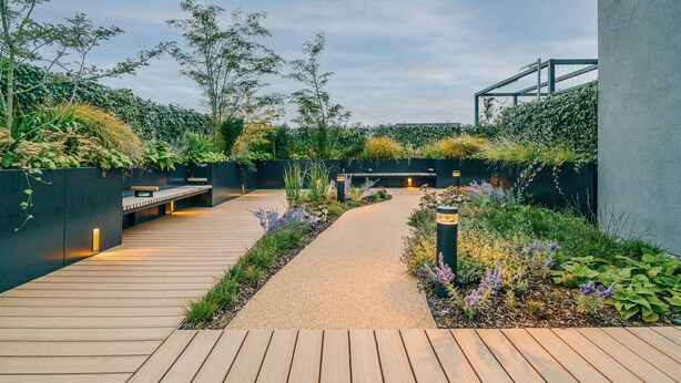 A wooden pathway leading to a seating area with a bench, surrounded by lush greenery and a wall with climbing plants. - City Apartments by Dublin At Home (Dublin)