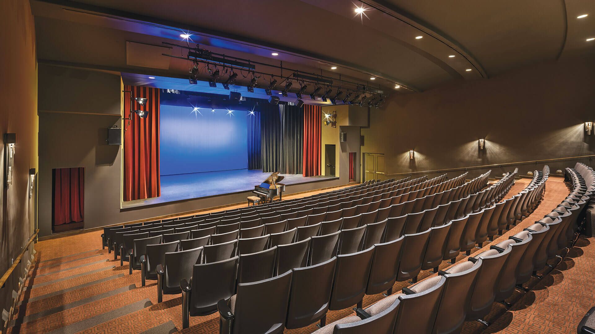 Un teatro con file di posti a sedere, un palco con tende e attrezzature per l'illuminazione.