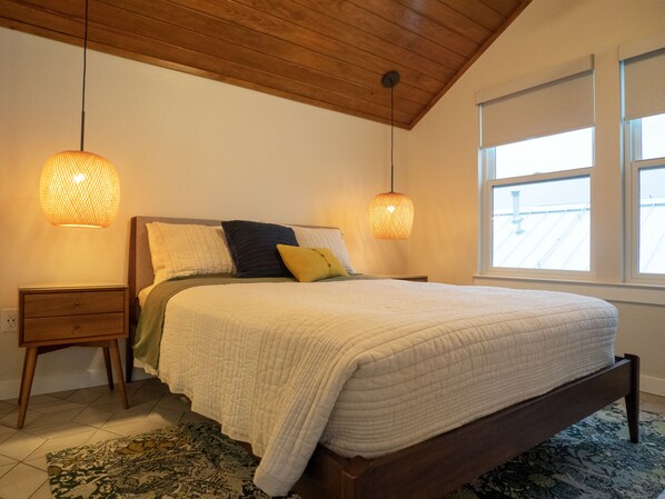 A bedroom with a wooden ceiling, a large bed with a white quilt, two bedside tables, and two hanging lamps. - Gorgeous, one-bedroom garage apartment in a quiet neighborhood (Austin)
