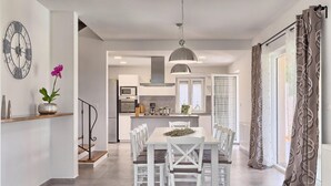 Een moderne keuken met witte kasten, een eettafel met stoelen, een hanglamp en een klok aan de muur.