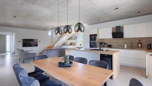 Una cucina moderna con isola centrale, elettrodomestici integrati e zona pranzo con tavolo in legno e sedie imbottite.
