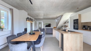 Una cucina moderna con isola in legno, sedie rivestite di grigio e un grande tavolo da pranzo.