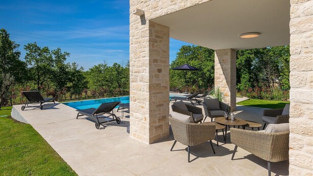 Area piscina esterna con lettini e una zona relax coperta con tavoli e sedie.