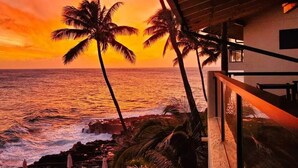 Vista do pôr do sol a partir de uma varanda com palmeiras e uma praia.