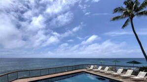 Área da piscina com espreguiçadeiras e guarda-sóis, com vista para o oceano.