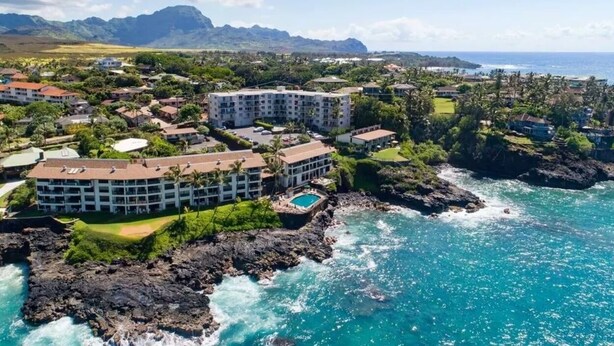 Um hotel à beira-mar com vários edifícios, uma piscina e vista para o oceano e montanhas.