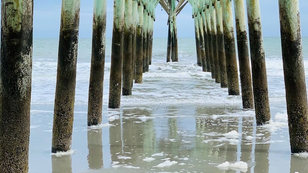 A pier with a series of wooden pillars supporting a roof, extending into the water. - ⛱ FABULOUS DIRECT OCEANFRONT KING BED⛱ ALL NEW RENOVATION! BALCONY! POOL VIEW ! (Myrtle Beach)