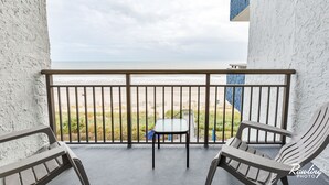 A balcony with two Adirondack chairs, a small table, and a view of the beach and ocean. - ⛱ FABULOUS DIRECT OCEANFRONT KING BED⛱ ALL NEW RENOVATION! BALCONY! POOL VIEW ! (Myrtle Beach)
