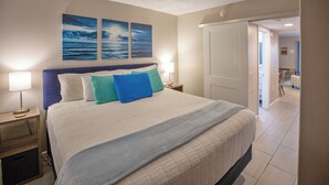 A bedroom with a bed, two bedside tables, a nightstand, and a door leading to another room. - ⛱ FABULOUS DIRECT OCEANFRONT KING BED⛱ ALL NEW RENOVATION! BALCONY! POOL VIEW ! (Myrtle Beach)