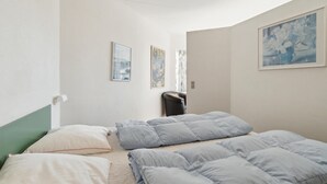 Un dormitorio con cama, almohadas, una silla y dos cuadros en la pared.