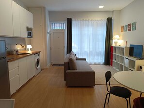 Cozy living space with a kitchenette, sofa, and dining area, featuring a washing machine and access to an outdoor area.