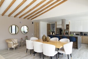 Une cuisine moderne avec des meubles blancs, un plafond en bois et un coin repas comprenant une table en bois et des chaises blanches.