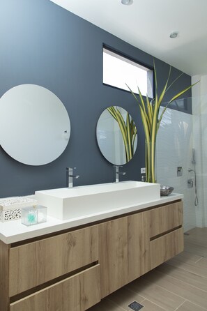 Modern bathroom with a round mirror, sleek sink, and wooden cabinets.