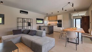 A modern living space with a grey sectional sofa, a wooden dining table with chairs, a kitchen area with a built-in oven, and a TV mounted on the wall. - Awesome home in Vodnjan (Vodnjan)
