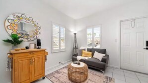 Un salon avec un canapé gris, un meuble en bois, une lampe sur pied et un tapis à motifs.