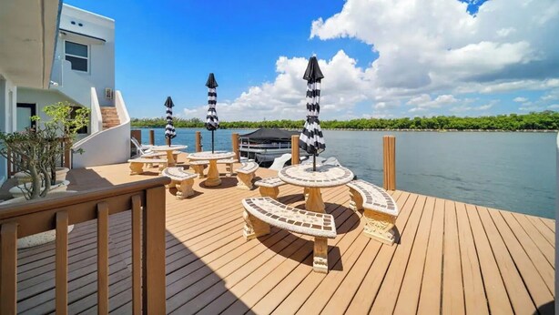 Une terrasse en bois avec des sièges et des parasols, offrant une vue sur une étendue d’eau calme et un ciel dégagé.
