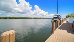 Une jetée en bois s’étendant sur des eaux calmes, sous un ciel dégagé, avec une côte lointaine à l’horizon.