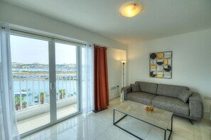 A modern living room with a sofa, a coffee table, and a view of a marina through large windows.