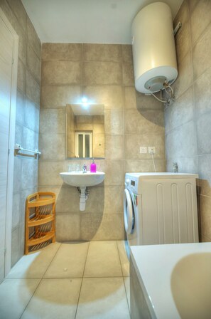 A bathroom with a sink, mirror, toilet, and a washing machine.