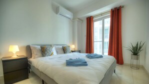 Une chambre à coucher moderne avec un grand lit, deux tables de chevet avec des lampes, une plante en pot et une fenêtre avec des rideaux.