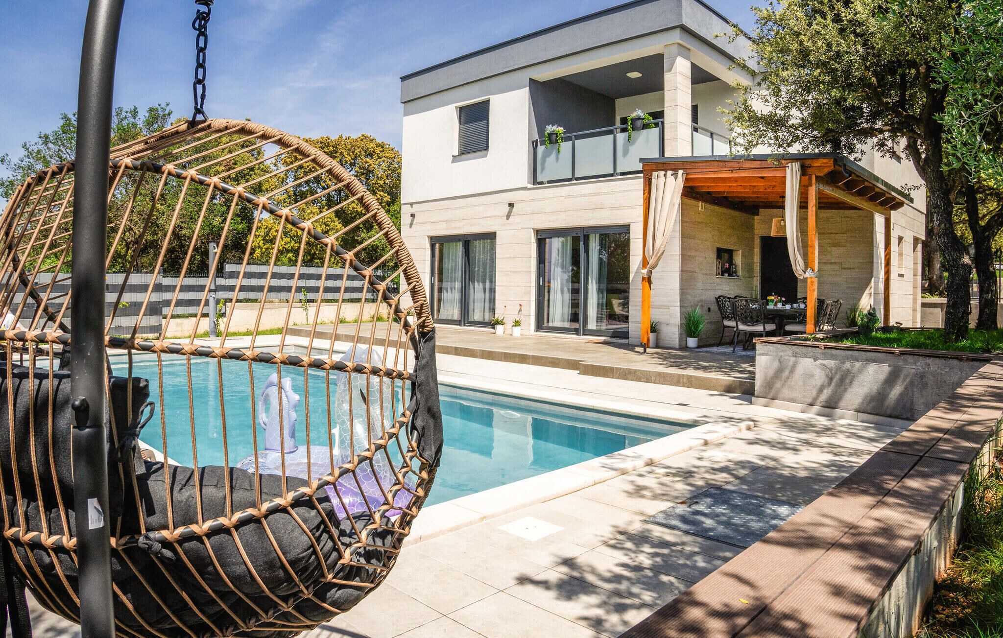 Una casa moderna con piscina, una hamaca colgante y un porche cubierto.