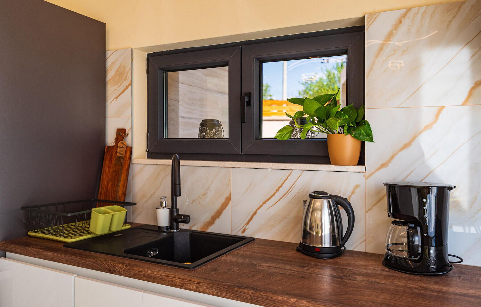 Eine Küche mit schwarzem Arbeitsplatz, Spüle, Fenster mit Pflanze und Kaffeemaschine.
