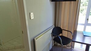 A hotel room with a TV mounted on the wall, a chair, a table, and a radiator. - Opuke Studio Methven (Methven)