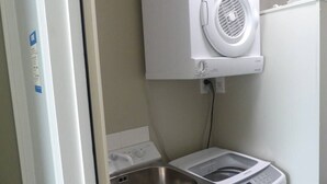A compact laundry area with a washing machine, a dryer, and a sink. - Opuke Studio Methven (Methven)