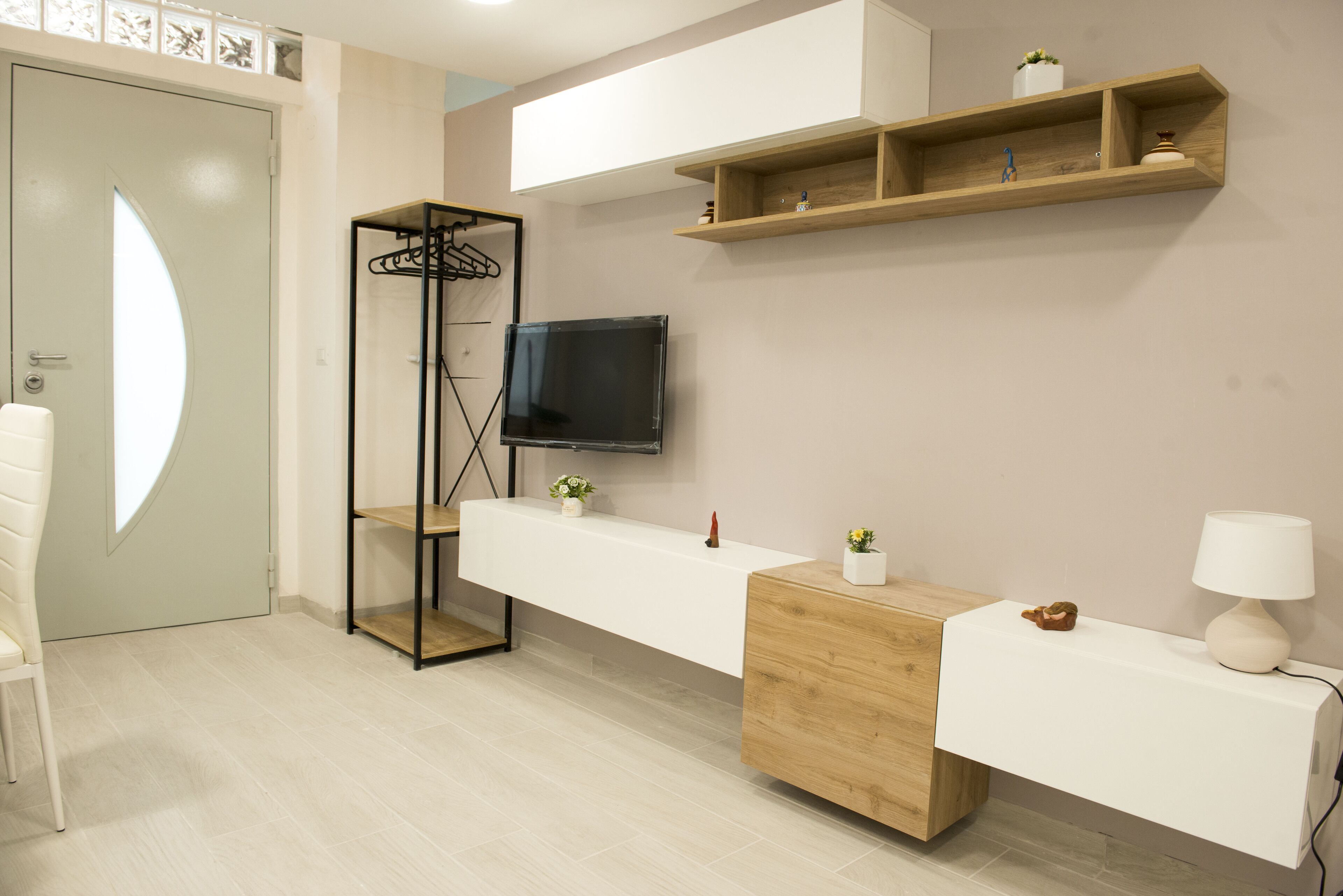 A modern room with a white sofa, a wooden cabinet, a TV mounted on the wall, and a wooden shelf with decorative items.