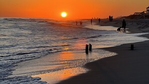 A beach at sunset with waves, a lifeguard tower, and people on the sand. - Family waterfront condo,Dog Friendly, pools, boat launch, beach access, WIFI! (Gulf Shores)