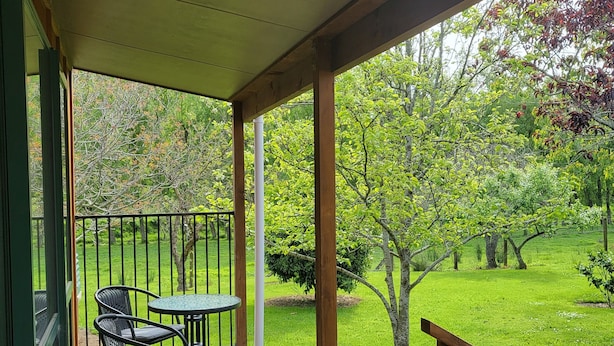A wooden deck with a table and chairs, overlooking a grassy yard with trees.